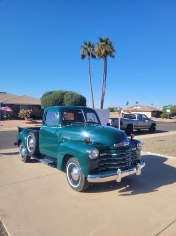 Shiny vintage green pickup truck parked in a suburban driveway under a clear blue sky